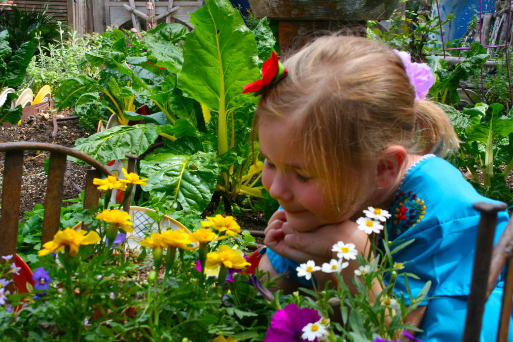 girl in garden flower bed smelling flowers